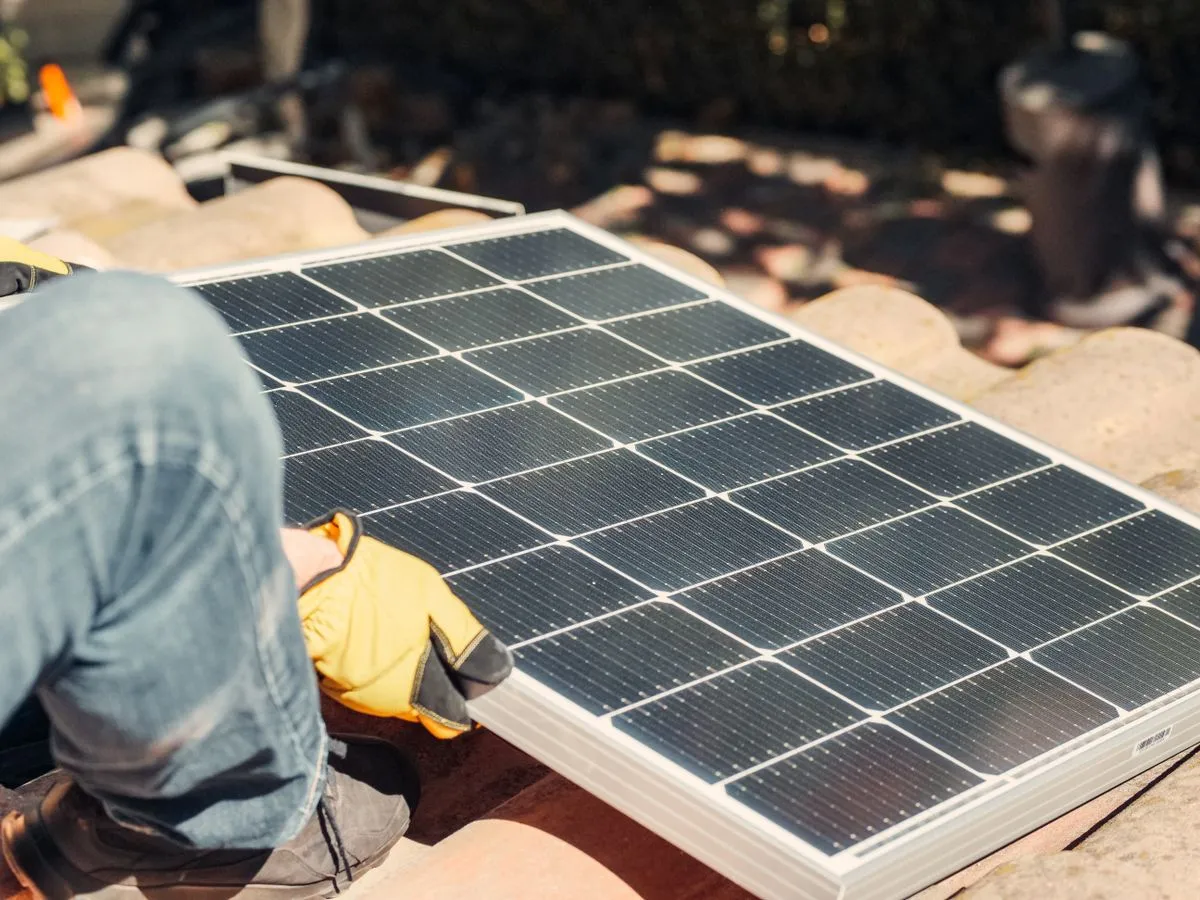 Installateur prüft Solarmodule auf einem Schrägdach mit Meer im Hintergrund
