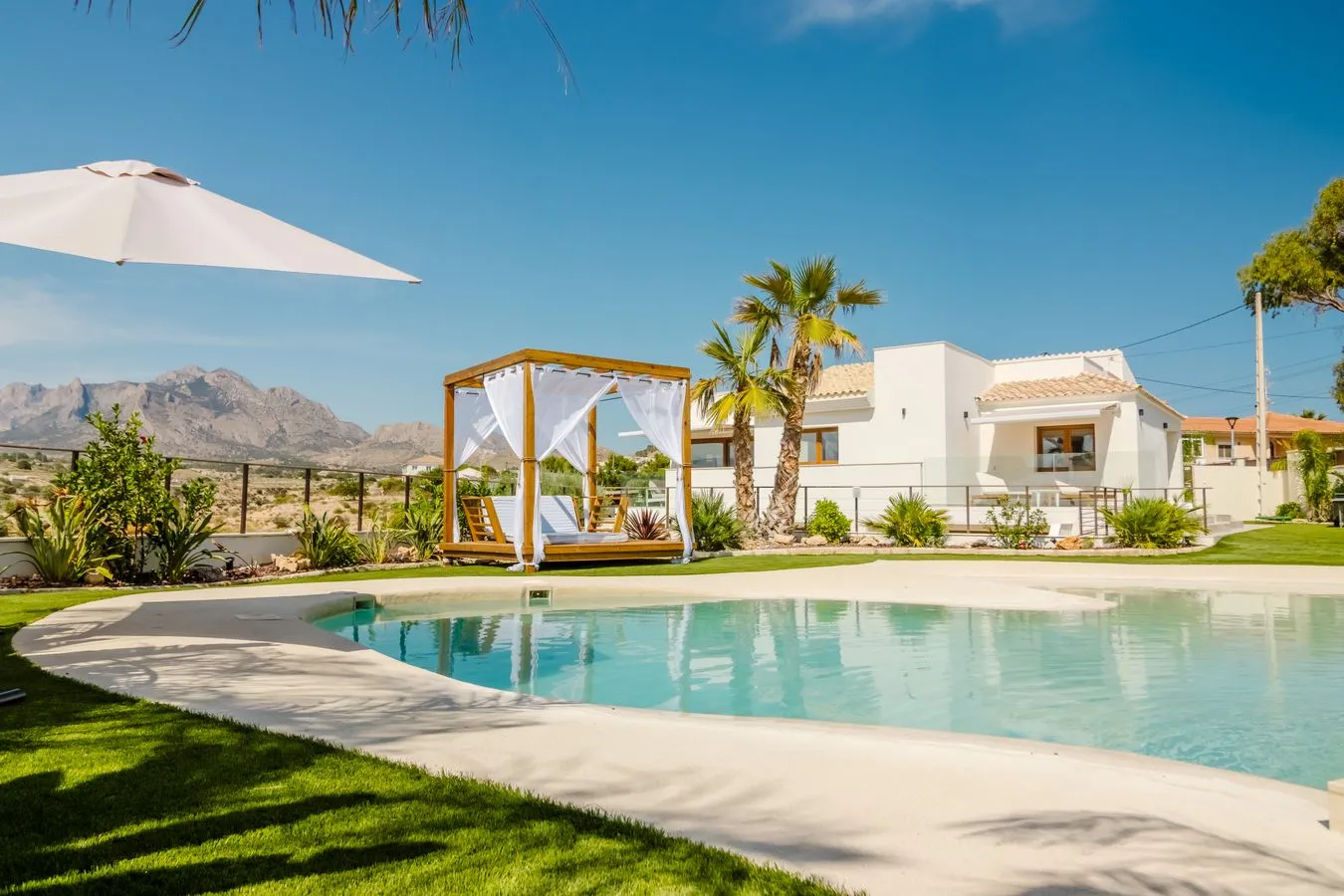 Weiße mediterrane Villa mit Pool und Palmen an einem sonnigen Tag
